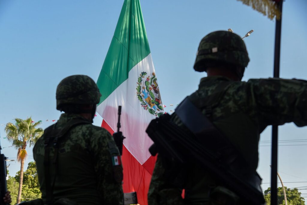 A group of uniformed Mexican military personnel march in formation during a festive parade